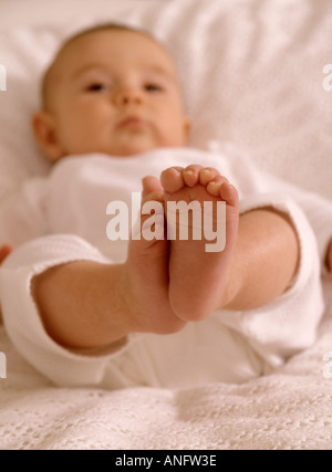 Babymädchen trägt einen Pyjama liegend mit den Füßen oben in der Luft Stockfoto