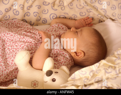 Babymädchen schläft in ihrem Bettchen mit einem Teddybär Stockfoto