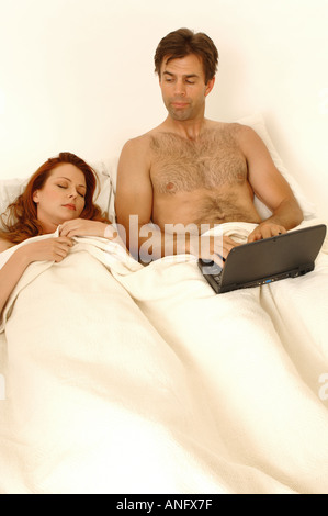 Porträt eines Mannes mit seinem Laptop im Bett, während seine Frau schläft Stockfoto