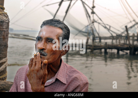 Benjamin, entspannt ein Fischer, der die traditionellen chinesischen Fischernetze in Fort Cochin verwendet mit einer Zigarette in den frühen Morgenstunden Stockfoto