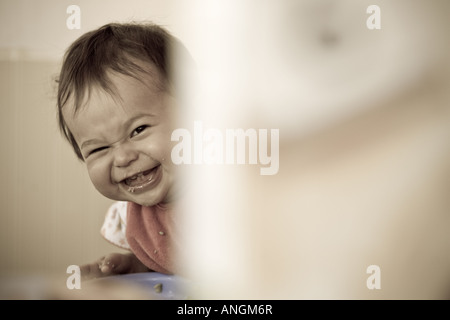 Kleines Mädchen lacht während des Spielens Peek ein Boo während einer Mahlzeit. Stockfoto