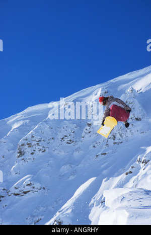 Junge weibliche Snowboarder springen von einem Gesims im Backcountry. Golden, British Columbia, Kanada Stockfoto