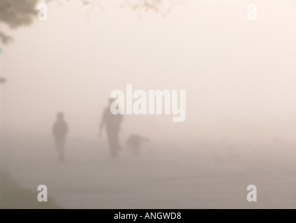 eine Familie nimmt den Hund für einen Spaziergang in den frühen Morgennebel am Strand Stockfoto