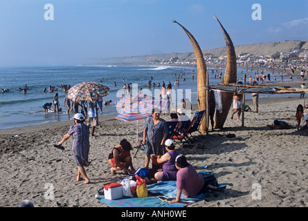 Reed Angelboote/Fischerboote (Caballitos de Totora) werden zum Trocknen in Huanchaco, Peru, gestapelt, wie Familien einen Urlaub am Strand genießen Stockfoto