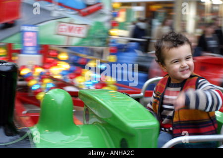 Kleiner Junge auf spannende Kreisverkehr fahren Weihnachts-Einkäufer und Fenster im Hintergrund anzeigen Stockfoto