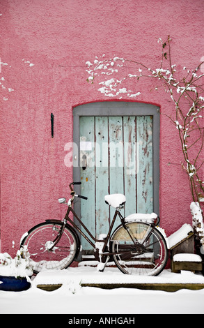 Ein verschneiter Wintertag in Presteigne, Powys, Wales, UK. Ein altes Fahrrad gegen eine rosa Wand lehnt Stockfoto