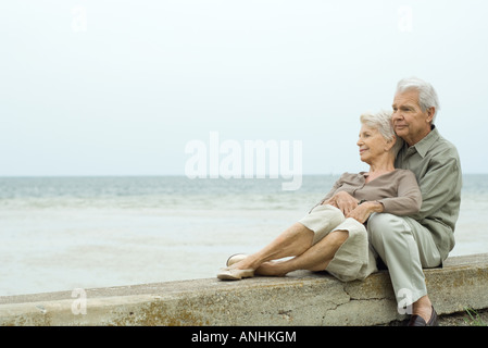 Älteres paar sitzen zusammen am Strand, umarmen, betrachten Stockfoto