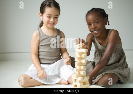 Zwei Mädchen sitzen am Boden spielen mit Blöcken, ein Lächeln in die Kamera Stockfoto