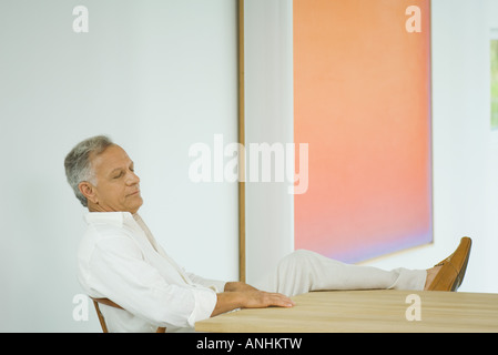Reifer Mann mit Bein, geschlossenen Augen am Tisch sitzen Stockfoto