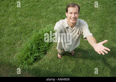 Mann stehend und Büschel Gras in einer Hand hält lächelnd in die Kamera, erhöhte Ansicht Stockfoto