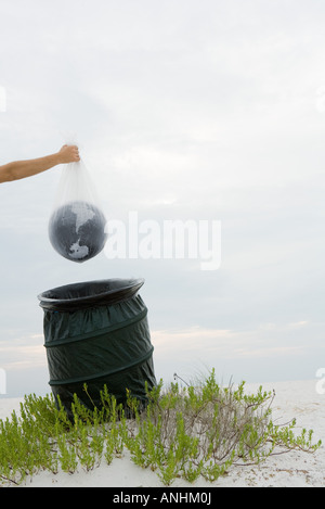 Person, die Welt in Plastiktüte über Mülleimer, verkürzte Ansicht Stockfoto