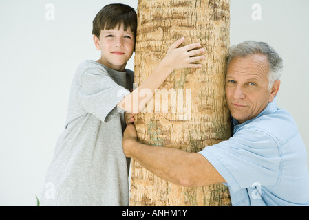 Großvater und Enkel umarmt Baumstamm, lächelnd in die Kamera Stockfoto
