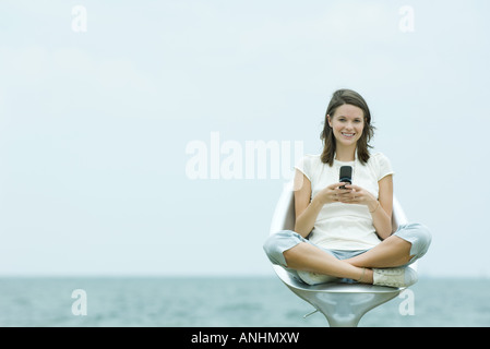 Teen Mädchen sitzend, mit Handy, Ozean Horizont im Hintergrund Stockfoto