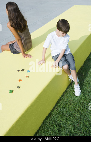 Bruder und Schwester sitzen Rücken an Rücken auf Mäuerchen neben Toys, erhöhte Ansicht Stockfoto