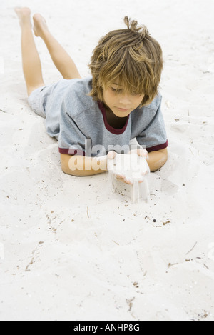Junge auf dem Boden liegend blickte auf Handvoll sand Stockfoto