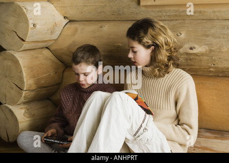 Teen Girl und preteen Boy sitzen nebeneinander, spielen und lesen Videospiel Stockfoto