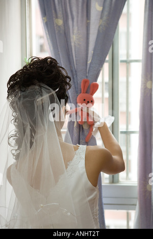 Braut vor Fenster, Vorhang mit Stofftier, Sicht nach hinten zu binden Stockfoto