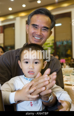 Mann Holding Kleinkind auf dem Schoß, klatschte, lächelnd in die Kamera Stockfoto