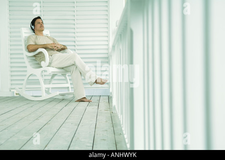 Mann sitzt im Schaukelstuhl auf der Veranda, Kopfhörer anhören Stockfoto