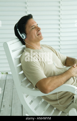 Mann sitzt im Schaukelstuhl, Kopfhörer anhören Stockfoto