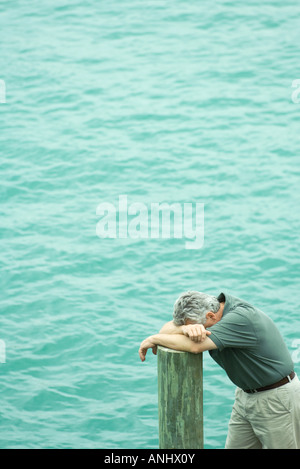 Man stützte sich auf Post, Kopf nach unten an Armen, erhöhte Ansicht, Wasser im Hintergrund Stockfoto