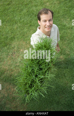 Mann hält Büschel Gras, lächelnd in die Kamera, erhöhte Ansicht Stockfoto