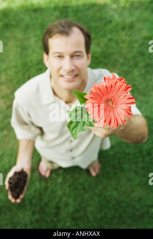 Mann hält Gerbera Daisy, lächelnd in die Kamera, erhöhte Ansicht Stockfoto