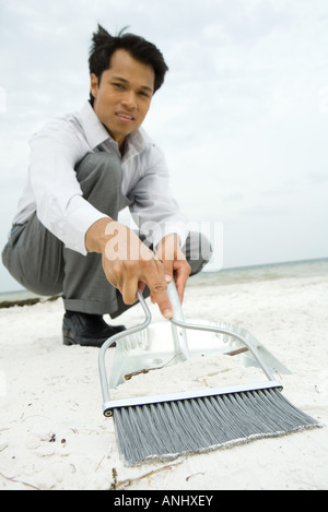 Mann am Strand, hockend fegen Sand ins Kehrschaufel, Blick in die Kamera, niedrigen Winkel Ansicht Stockfoto