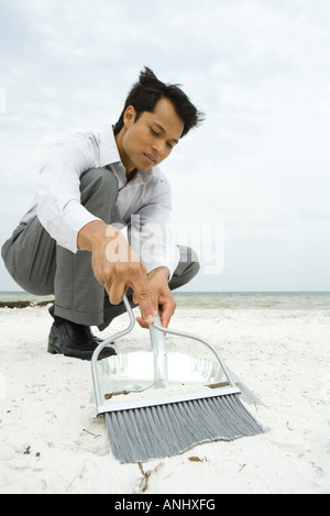 Mann am Strand, hockend fegen von Sand in der Schaufel, niedrigen Winkel Ansicht Stockfoto