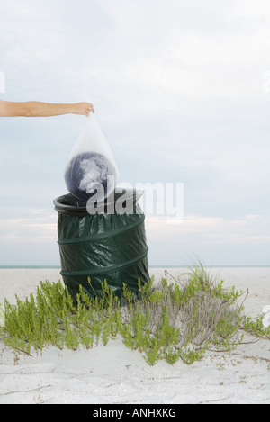 Person, die Welt in Plastiktüte über Mülleimer, verkürzte Ansicht Stockfoto