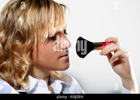 Frau, die Make-up mit einem flauschigen Pinsel aufträgt, sich auf ihr Gesicht mit einem neutralen Hintergrund fokussiert, zeigt eine Schönheitsroutine. Stockfoto