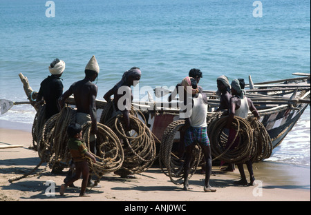 Nolia-Fischer, die ihre traditionellen weißen Hüte tragen, starten ein kleines Fischerboot in den Indischen Ozean vor der Küste von Odisha, Puri, Indien Stockfoto