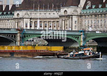 Ein Schlepper abschleppen cargo Schiff geht unter die Westminster Bridge, London, UK. Die alte County Hall Gebäude im Hintergrund Stockfoto