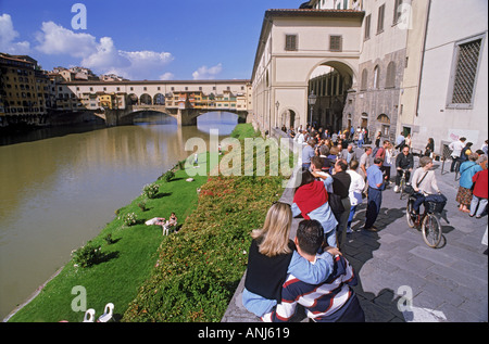 Menschen zu Fuß, in der Nähe von Radfahren und auf Mauer sitzend Uffizi Galerie am Fluss Arno in Florenz Stockfoto