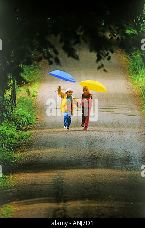 Jungen und Mädchen laufen auf Landstraße in den Regen halten Sonnenschirme Stockfoto