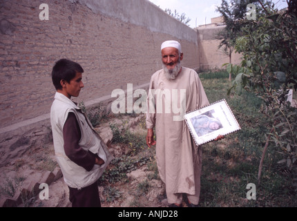 Der Hausmeister des Europäischen Friedhofs halten ein Bild von Brettina Goislard, während sein Sohn am Kabul Afghanistan 2003 sieht Stockfoto