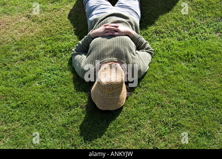 Eine Frau, die auf dem Gras und schlief in der Sonne mit ihren Hut über ihr Gesicht, an einem Dorffest in Herefordshire, UK Stockfoto