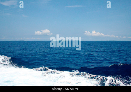 Weißer Schaum, verursacht durch den Durchgang eines Bootes in der Andaman See, gesäumt von einer Silhouette des Landes gegen eine Wolke übersät-Himmel Stockfoto