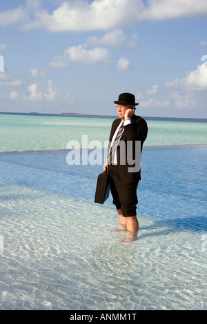 Malediven Überhitzung westliche Geschäftsmann in Bowler-Hut und Business Anzug auf Handy gekleidet stand im Schwimmbad Stockfoto