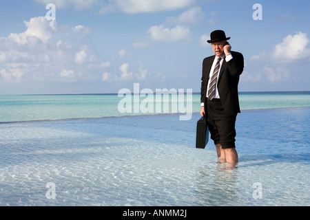 Malediven Überhitzung westliche Geschäftsmann in Bowler-Hut und Business Anzug auf Handy gekleidet stand im Schwimmbad Stockfoto