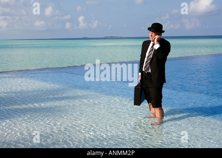 Malediven Überhitzung westliche Geschäftsmann in Bowler-Hut und Business Anzug auf Handy gekleidet stand im Schwimmbad Stockfoto