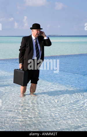 Malediven Überhitzung westliche Geschäftsmann in Bowler-Hut und Business Anzug auf Handy gekleidet stand im Schwimmbad Stockfoto