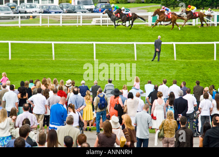 Horizontale Ansicht von Zuschauern gegen die Schienen gerade Pferde und Jockeys Rennen ging an einem sonnigen Tag Stockfoto