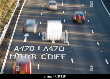 Horizontale Nahaufnahme von Straßenmarkierungen und Ortsnamen auf der M4-Autobahn in Richtung Cardiff mit Autos Beschleunigung entlang in der Sonne Stockfoto