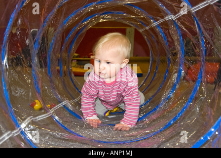 Horizontale Nahaufnahme von einem hübschen kaukasischen Babymädchen kriechen durch einen durchsichtigen Plastikschlauch in eine Krabbelgruppe Stockfoto