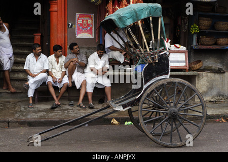 Eine Rikscha steht auf einer der Straßen in der Nähe von Kali Ghat in Kolkata, Indien. Die Rikscha-Puller sitzen in der Nähe, Tee zu trinken. Stockfoto