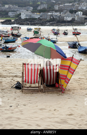 Ein Mann sitzt in einem Liegestuhl am Strand von St Ives Hafen bei Ebbe Cornwall England Stockfoto