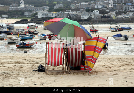 Ein Mann sitzt in einem Liegestuhl am Strand von St Ives Hafen bei Ebbe Cornwall England Stockfoto