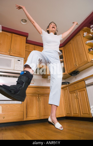 Niedrigen Winkel Blick auf eine Frau mittleren Alters mit Fußverletzung springen in der Küche und lachen Stockfoto