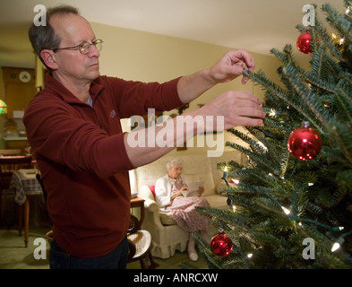 Bridgewater Virginia John West 61 schmückt einen Weihnachtsbaum, während seiner 100 Jahre alte Mutter in der Nähe sitzt Stockfoto
